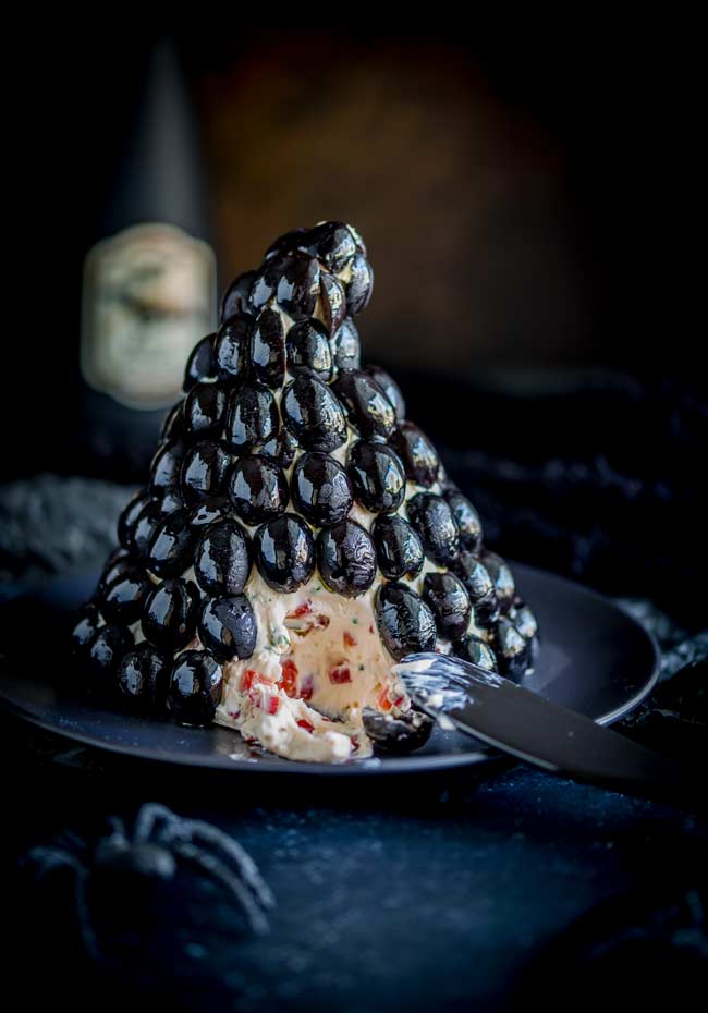 a black olive covered cheese ball shaped like a hat, with a section removed so you can see the creamy filling