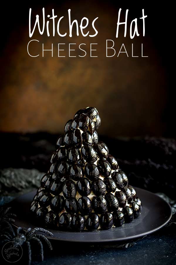 rusty back drop with a black olives crusted witches hat cheese ball on a black plate.