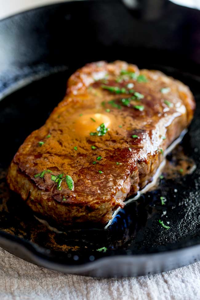 a ribeye steak in a cast iron pan with butter melting over it.