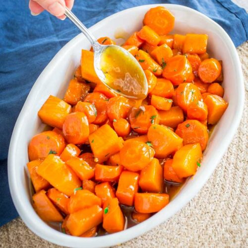sq picture showing the glaze being drizzled over a white dish of carrot and pumpkin