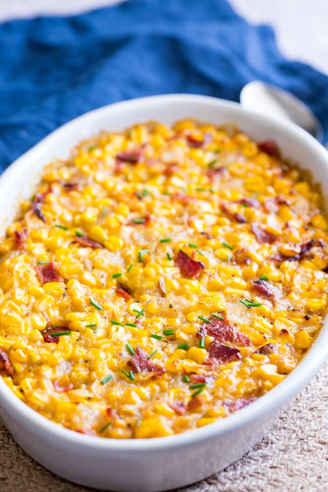 overhead of a white oval casserole dish filled with yellow corn casserole and garnished with bacon and chives