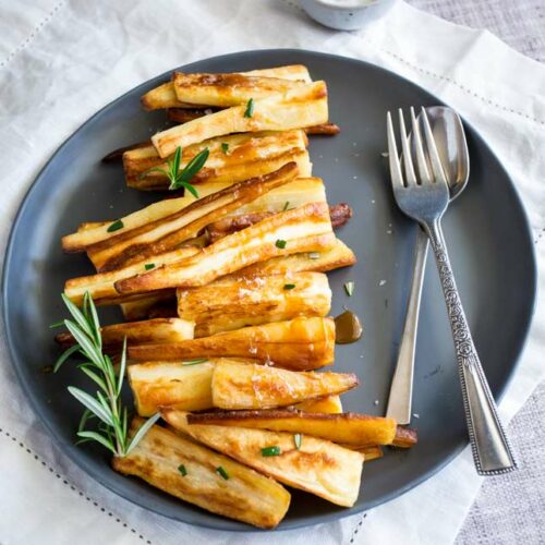 sq picture showing a grey plate with parsnips line up on it with a drizzle of caramel sauce and sprigs of rosemary