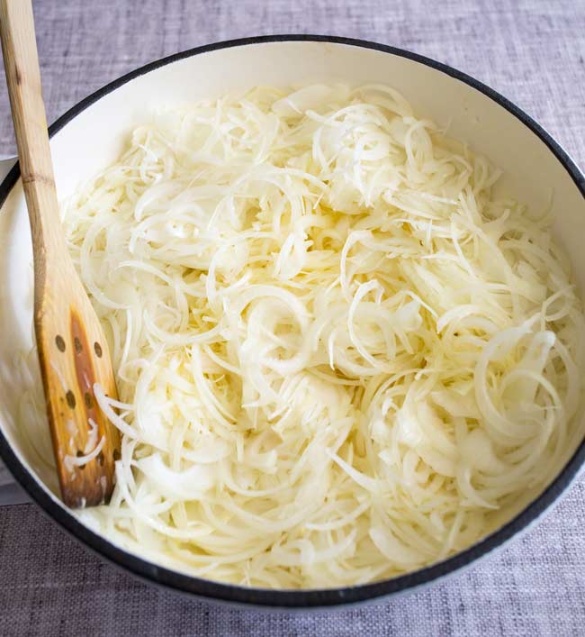 sliced onions in a white shallow cast iron pan on a grey table
