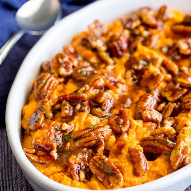 oval dish filled with sweet potato mash topped with pecans and maple syrup