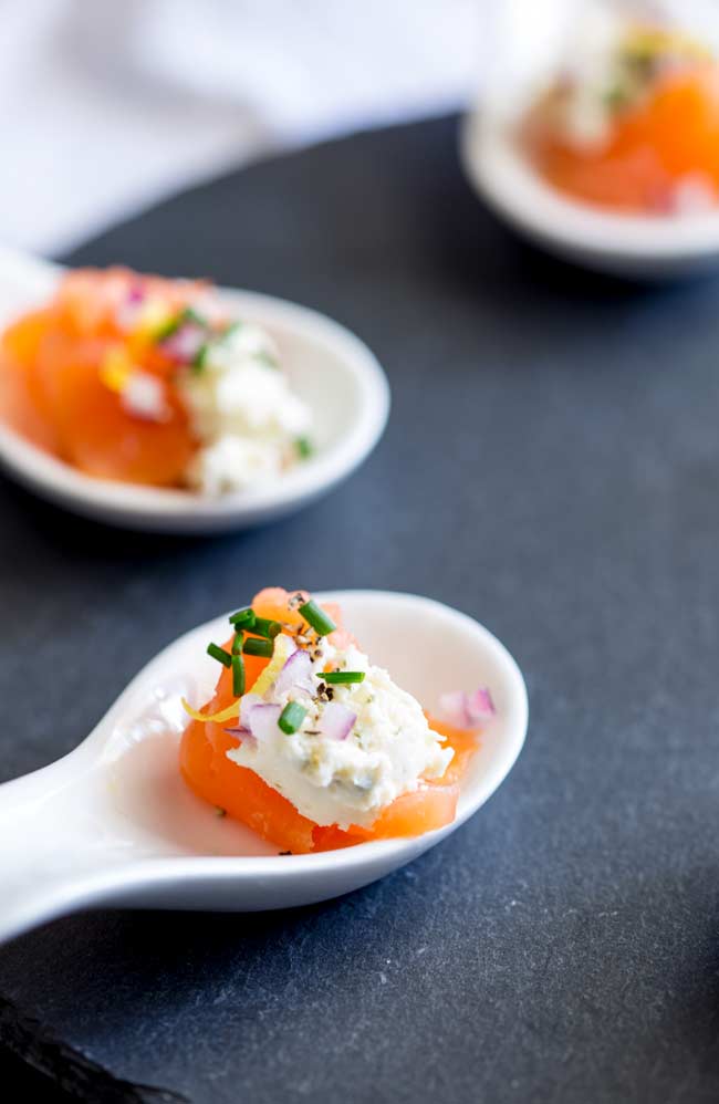a white amuse spoon on a slate tray filled with smoked salmon and cream cheese