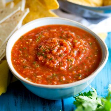 close up on the homage salsa in a small white bowl with chips behind it