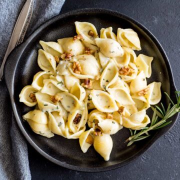 overhead close up of a black plate of creamy pasta with a rosemary sprig