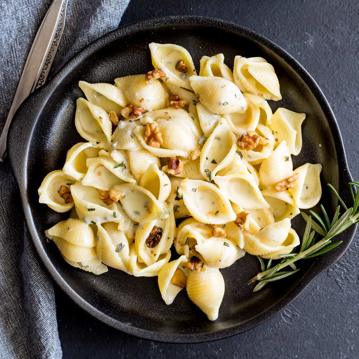 overhead close up of a black plate of creamy pasta with a rosemary sprig