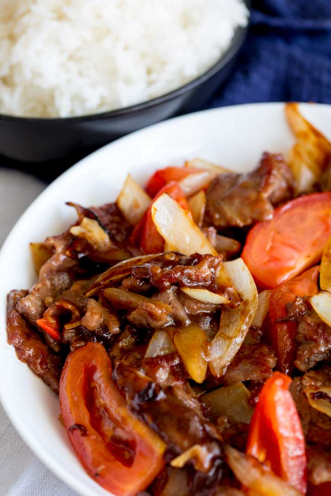 Cantonese beef and tomato stir fry in a white bowl with rice in the background