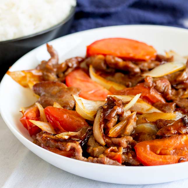 square image of a white bowl cantonese style beef and tomatoes