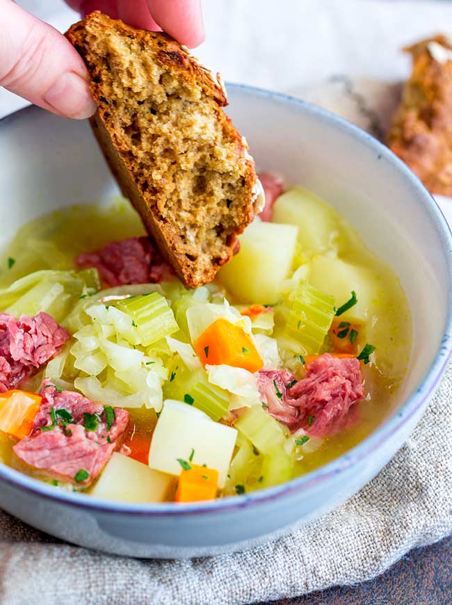 soda bread being dipped into a bowl of corned beef and cabbage soup