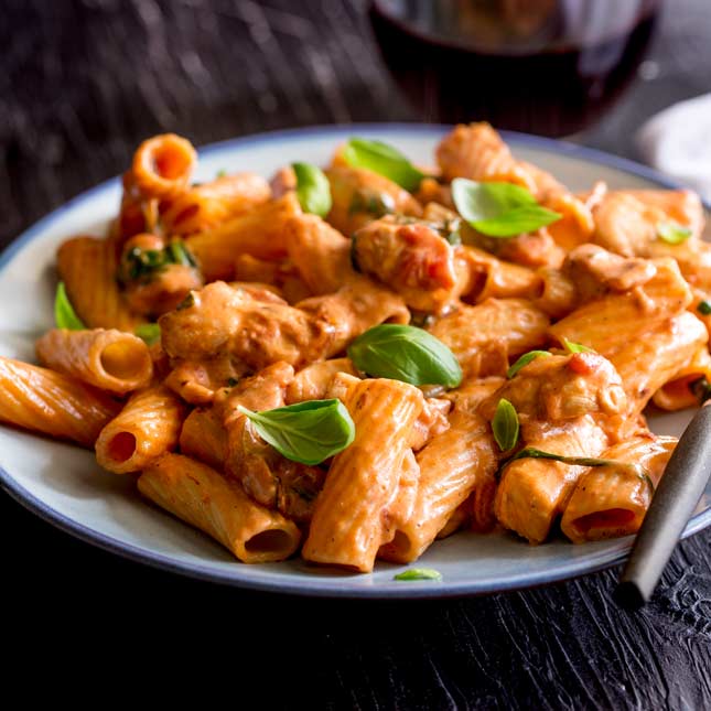 a pale blue plate with rigatoni pasta in a cream tomato sauce garnished with basil