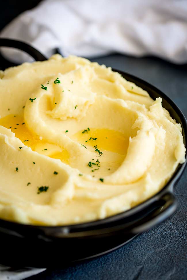 close up on a black bowl of french style mashed potato garnished with melted butter and parsley