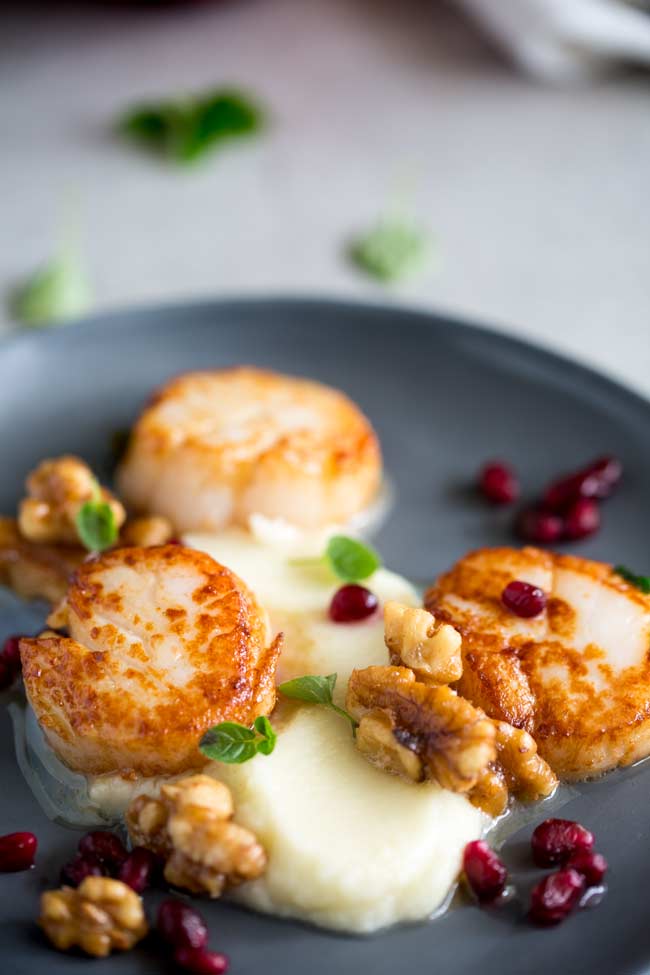 overhead view showing the seared scallops with cauliflower puree and the walnut butter and pomegranate arils 