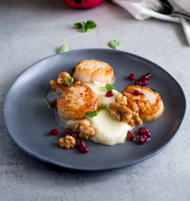 a grey plat eon a grey table with seared scallops and cauliflower puree