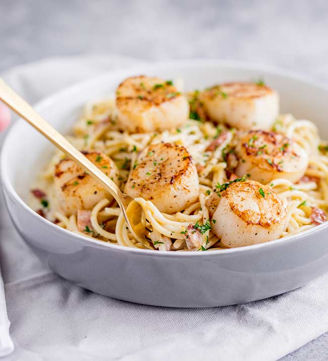 a grey bowl full of bacon spaghetti with seared scallops on top