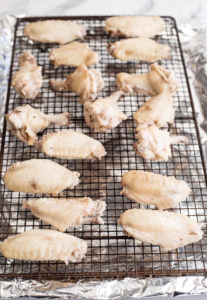 white poached chicken wings on a grid rack ready for the oven