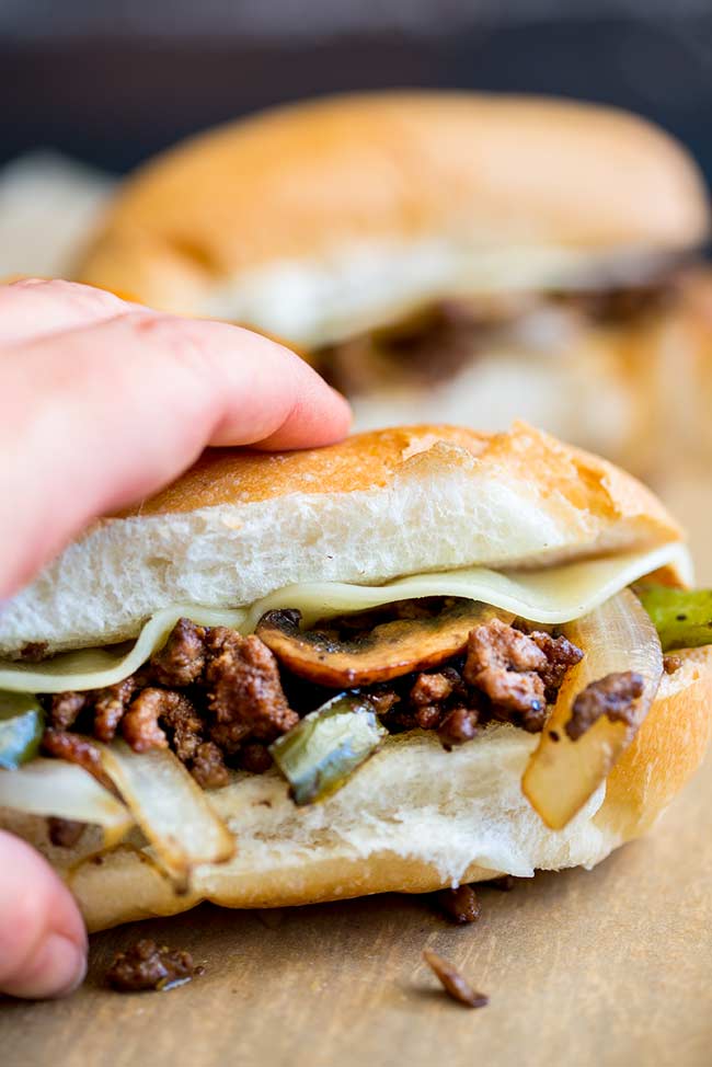 a hand picking up a ground beef Philly Cheesesteak sandwich