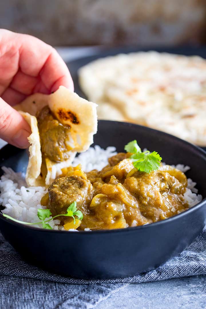 a hand using a piece of naan bread to scoop up lamb Dopiaza curry
