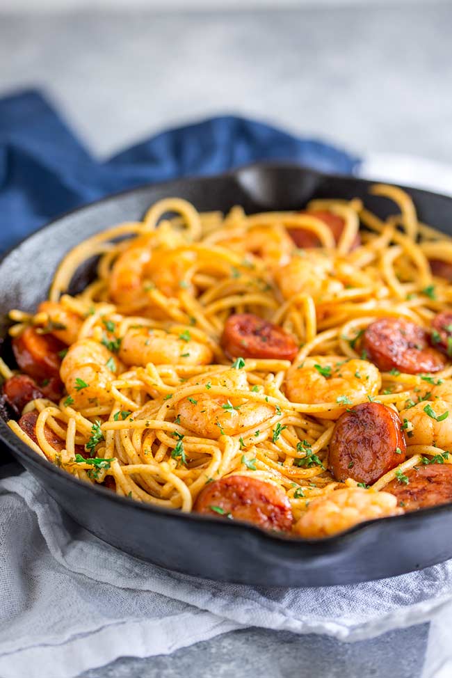 table view of a black cast iron skillet, on a white table cloth, filled with orange shrimp chorizo spaghetti and garnish with parsley