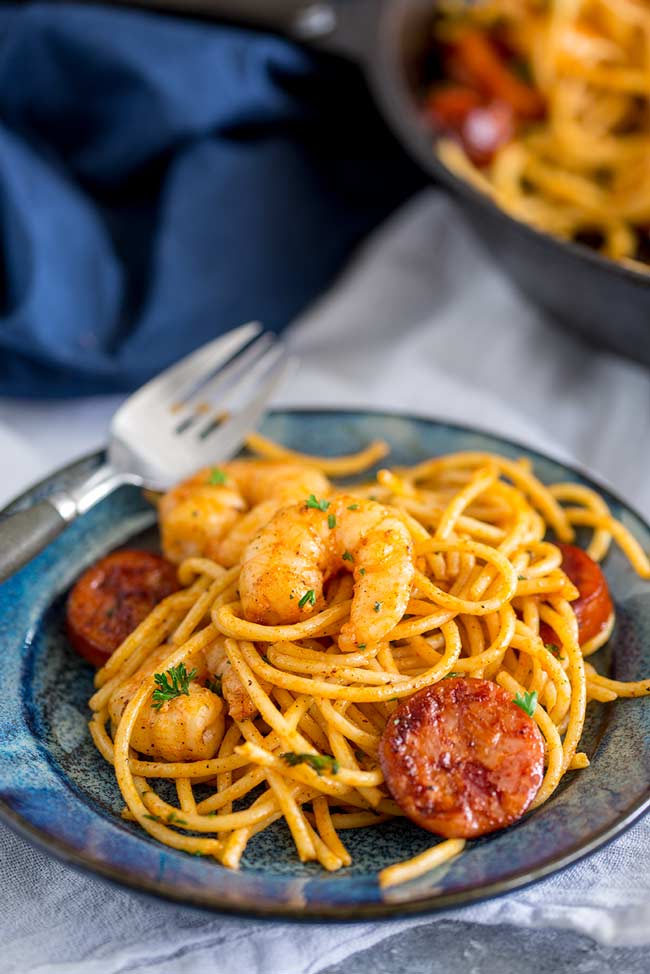a blue plate oiled with orange shrimp chorizo pasta with a pan of pasta in the background