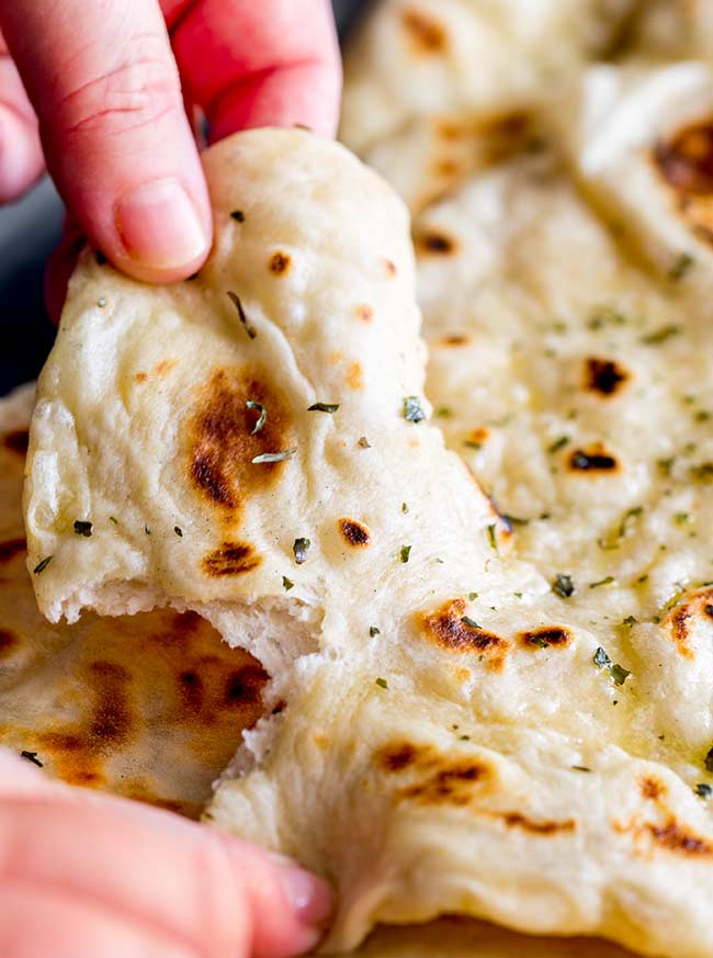 a hand ripping a piece of garlic naan bread off a large piece