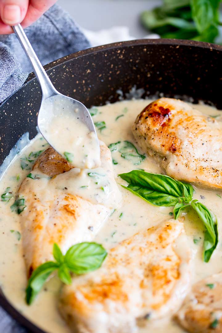 a creamy basil sauce being spooned over a chicken breast