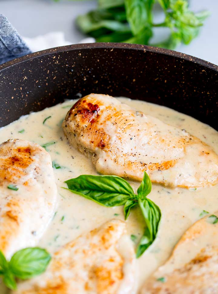 4 chicken breasts in a black skillet with a creamy basil sauce