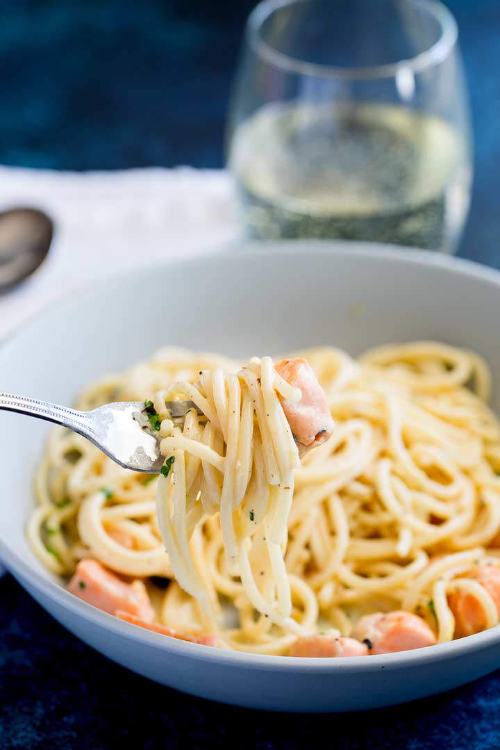 a silver fork picking up creamy lemon salmon pasta from a grey bowl