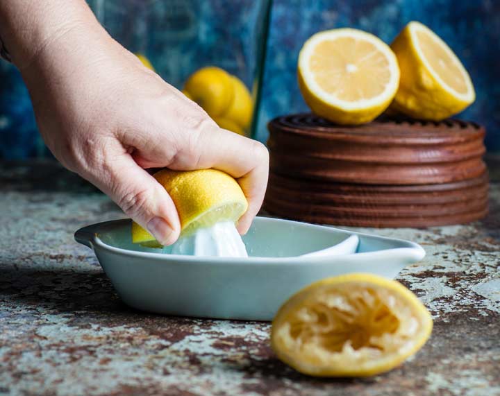 half a lemon being juiced on a ceramic juicer with cut lemons scattered around