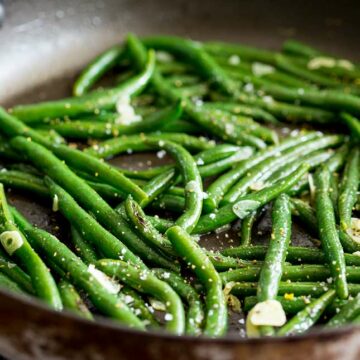 overhead view of a large black skillet with green beans and garlic