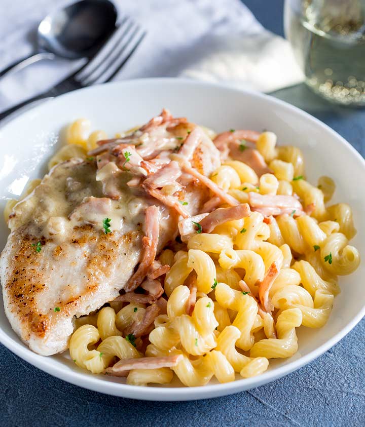 white bowl of spiral pasta with a chicken breast on top, on a blue table