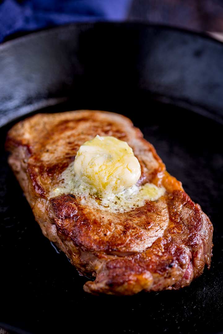 a seared steak in a cast iron skillet with a round of butter melting on it