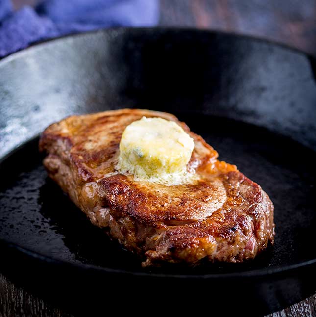 a steak in a black skillet with some butter melting over it