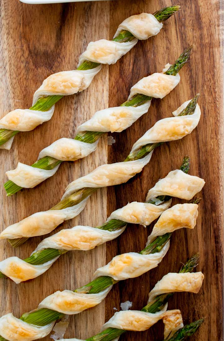 6 spears of asparagus wrapped in puff pastry on a wooden board