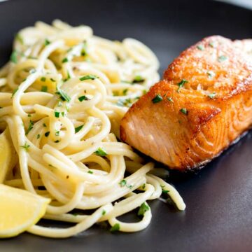 close up on the crispy salmon and pasta on a black plate