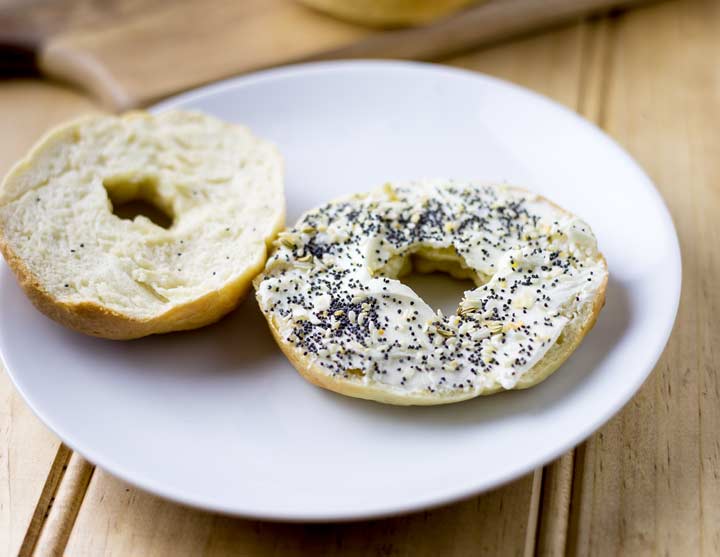 a cut bagel on a white plate, spread with cream cheese and everything seasoning 