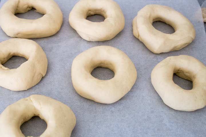7 uncooked bagels on a sheet of parchment paper