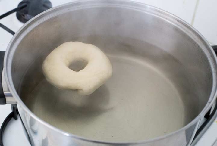 a bagel being poached in a pan of boiling water