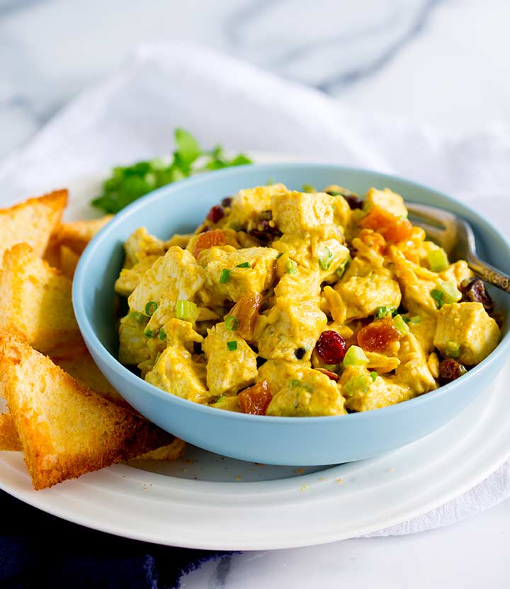 a blue bowl full of curry chicken salad with toast points on the side