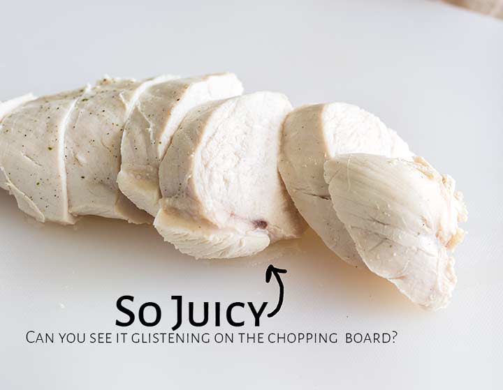 a sliced poached chicken breast on a white chopping board