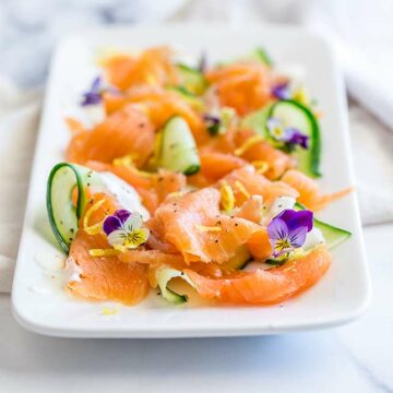 retangular platter of smoked salmon curls and cucumber ribbons on a marble countertop