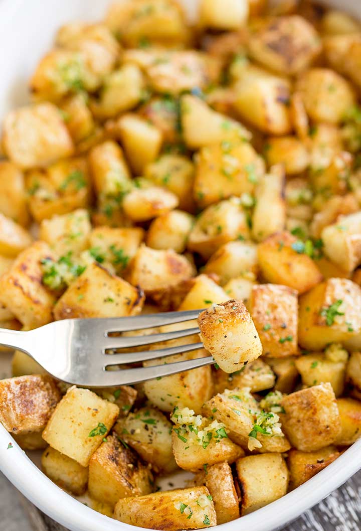 overhead view of a dish of crispy garlic butter potatoes with a fork picking one up