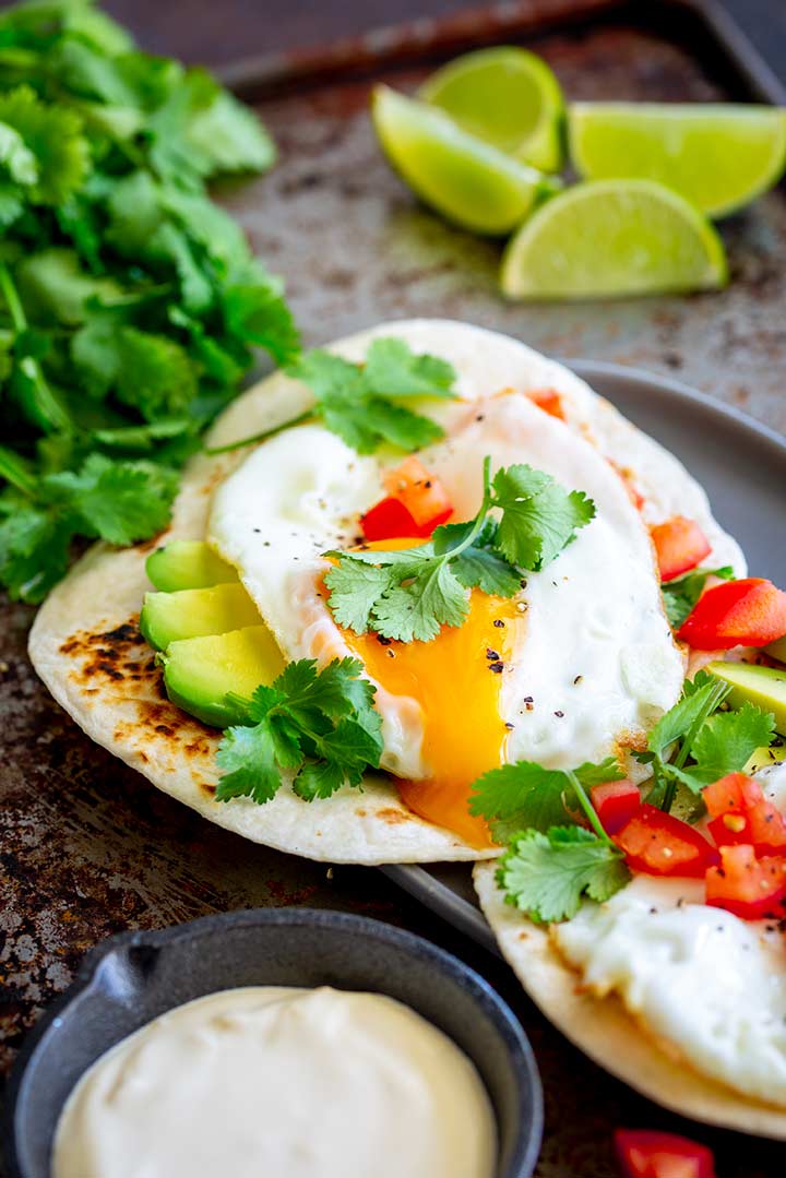 a fried egg with a runny yolk flowing over avocado filled tortilla
