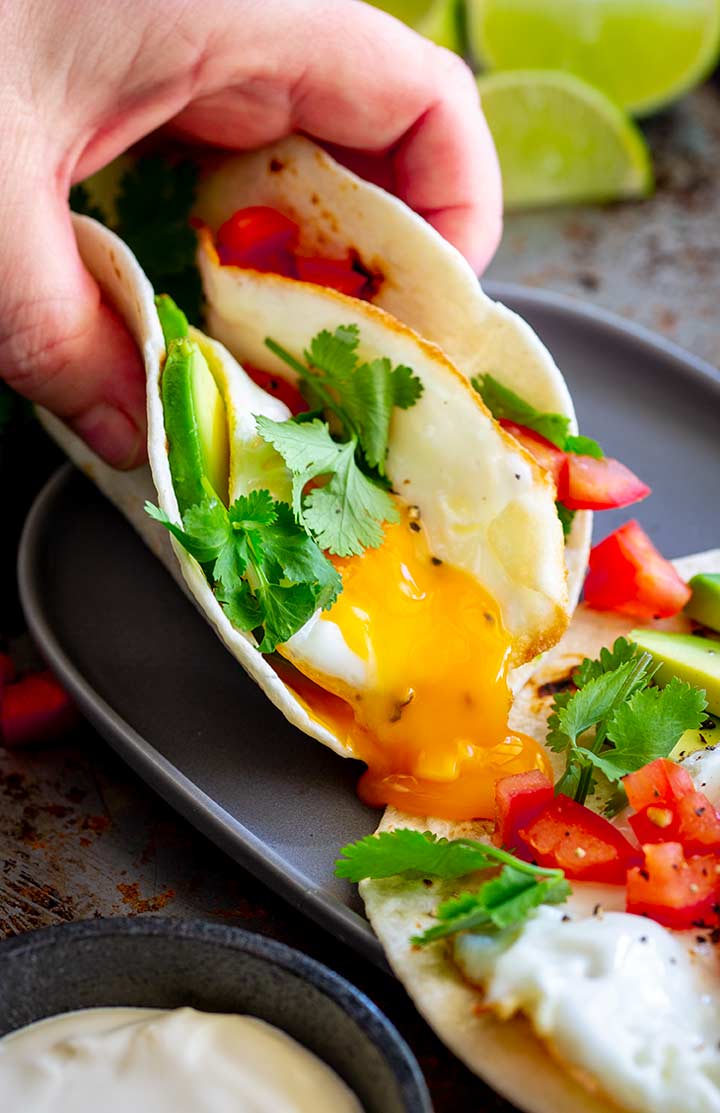 A hand picking up an egg taco as the runny yolk spills out