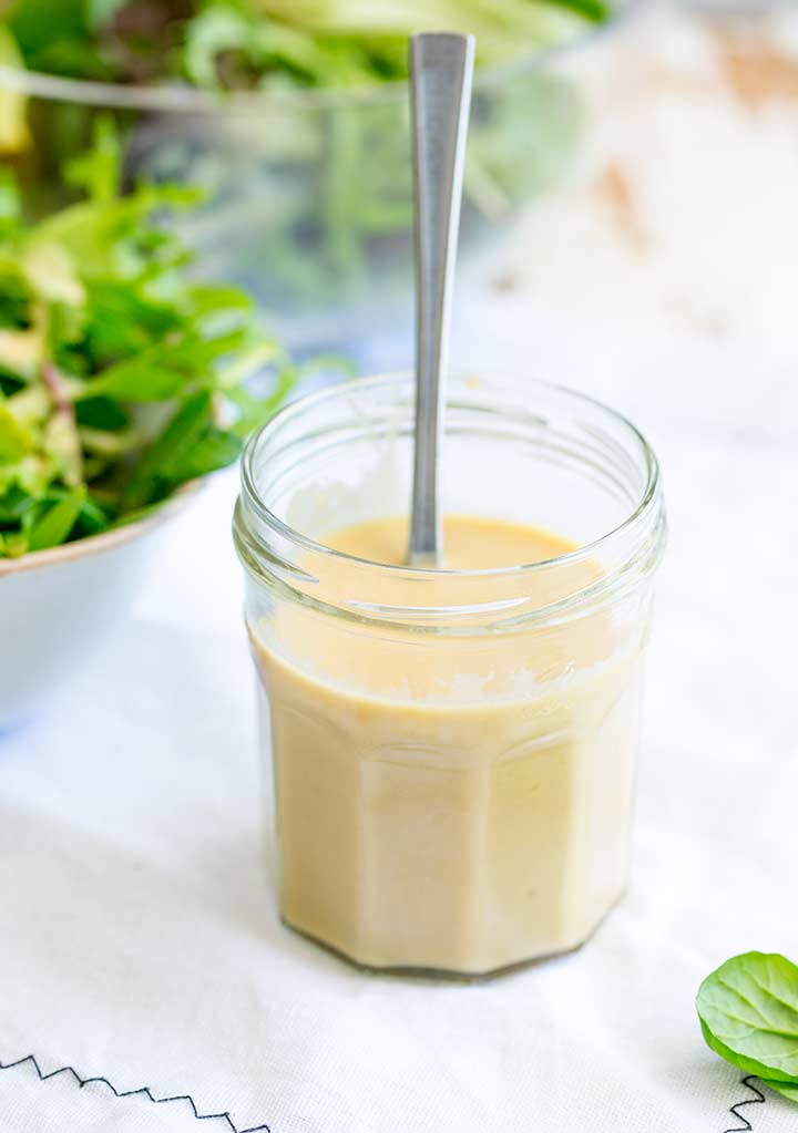 a class jar of hummus salad dressing with a spoon in it
