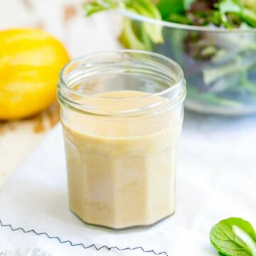 close up of a jar of hummus salad dressing on a white table
