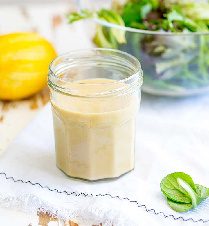 glass jar of creamy dressing with a bowl of salad in the background
