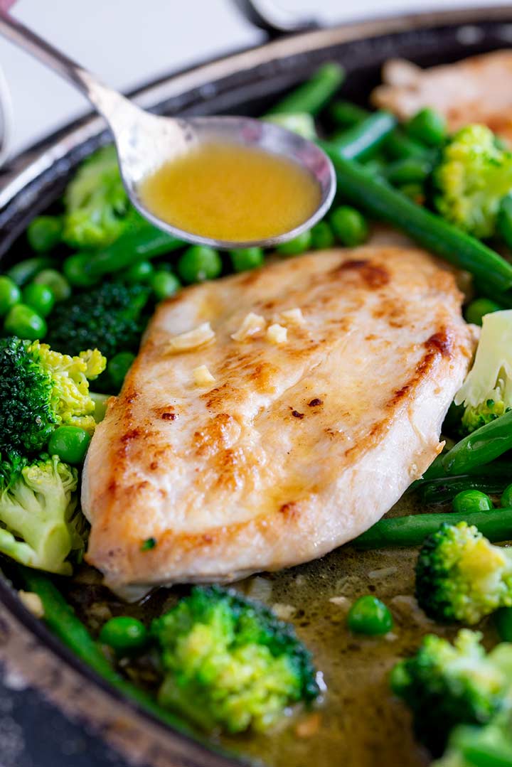 garlic butter being spooned over a pan of chicken breasts and vegetables