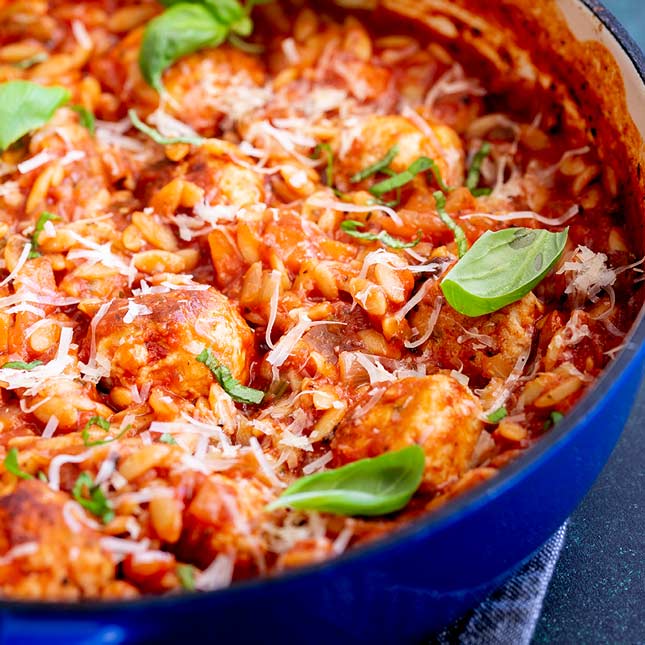 close up on the edge of a blue casserole full of meatball orzo